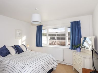 A bedroom with a bed striped bedding blue curtains a dresser with a mirror and a plant at Neaudd Wen Red Wharf Bay near Benllech