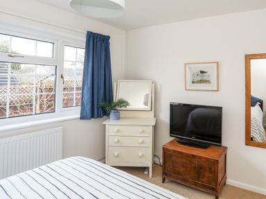 A bedroom with a window blue curtain a white dresser with a mirror and plant a wooden table with a tv and a framed bird picture on the wall at Neaudd Wen Red Wharf Bay near Benllech
