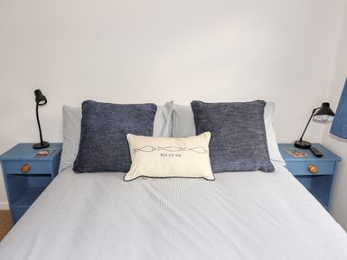 A bed with two large blue cushions and a small pillow with fish design and text sea la vie between two blue bedside tables with lamps and books at Neaudd Wen Red Wharf Bay near Benllech