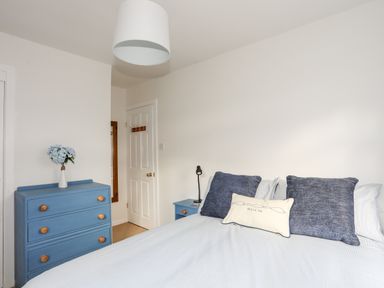 A bedroom with a bed with blue and white pillows a blue chest of drawers with a vase of flowers and a white door at Neaudd Wen Red Wharf Bay near Benllech