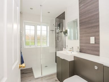 A bathroom with a glass shower enclosure a sink with cabinets and a window at Neaudd Wen Red Wharf Bay near Benllech