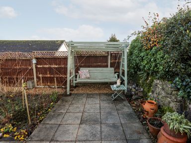An outdoor patio with a wooden swing bench a small folding table with decorations potted plants and a wooden fence