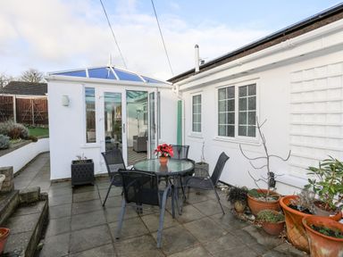 An outdoor patio area with a glass table and four chairs near a white conservatory at Neaudd Wen in Red Wharf Bay near Benllech