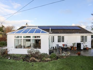 A white bungalow with a glass conservatory and patio furniture in the backyard at Neaudd Wen in Red Wharf Bay near Benllech