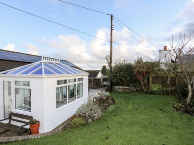 A garden with grass shrubs trees and a white conservatory attached to a house at Neaudd Wen Red Wharf Bay near Benllech