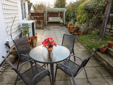A patio area with a glass table and four chairs and a potted plant on the table at Neaudd Wen in Red Wharf Bay near Benllech
