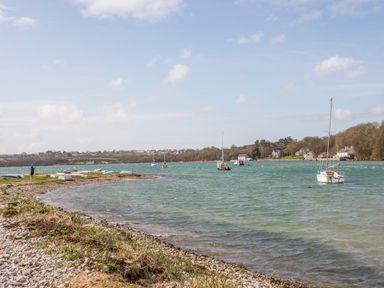 A shoreline with boats on water and houses in the background at Neaudd Wen Red Wharf Bay near Benllech