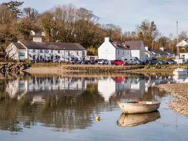 A small boat on calm water near a shoreline with white buildings cars and trees at Neaudd Wen Red Wharf Bay near Benllech