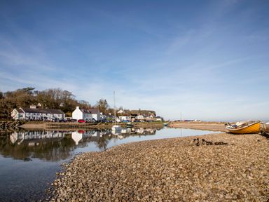 A rocky shore with boats on the water and white houses along the shoreline at Neaudd Wen Red Wharf Bay near Benllech