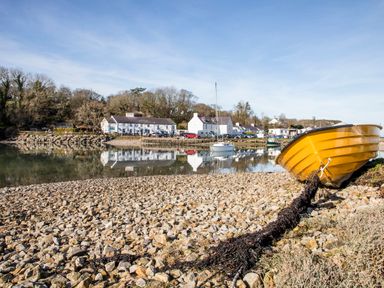A yellow boat on a rocky shore with houses and boats reflecting on calm water at Neaudd Wen Red Wharf Bay near Benllech