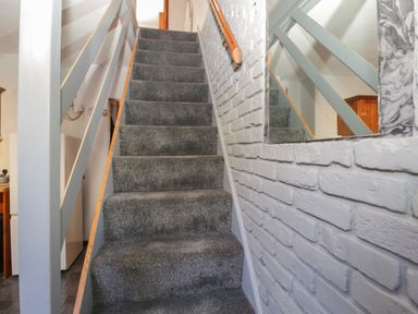 A carpeted staircase with a wooden handrail and a white brick wall with a mirror at Saddlers Cottage in Weymouth
