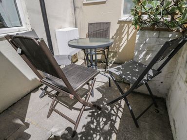 A small outdoor patio area with a round glass table and three chairs at Saddlers Cottage in Weymouth