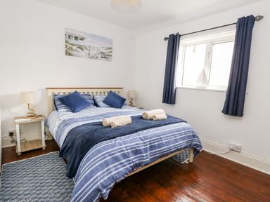 A bedroom with a double bed striped bedding and rolled towels two bedside tables with lamps a window with curtains and a painting on the wall at Saddlers Cottage in Weymouth