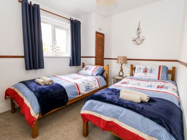A bedroom with two single beds with patterned bedding and rolled towels by a window at Saddlers Cottage in Weymouth