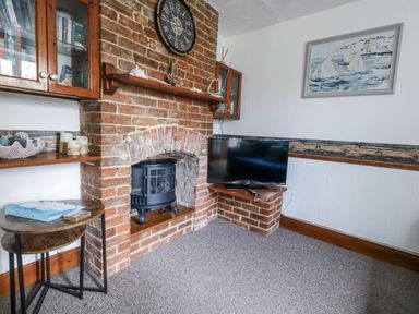 A living room with a brick fireplace and television at Saddlers Cottage in Weymouth