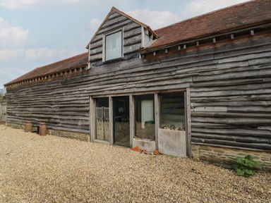 An exterior view of a wooden barn with gravel ground and small windows at Brandeers Long Barn in Brandier near Minety