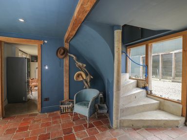 A corner with a blue wicker chair hats hanging on a branch and stone spiral stairs next to a window at Brandeers Long Barn Brandier near Minety