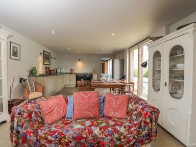 An open plan kitchen and dining area with a patterned sofa and wooden dining table at Brandeers Long Barn in Brandier near Minety