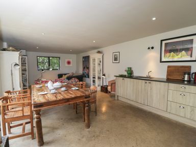 A kitchen and dining area with a wooden table and chairs cupboards and a living area at Brandeers Long Barn in Brandier near Minety