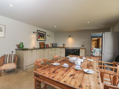 A kitchen with wooden table set for tea wooden chairs light wood cabinets black stove and stainless steel refrigerator at Brandeers Long Barn in Brandier near Minety