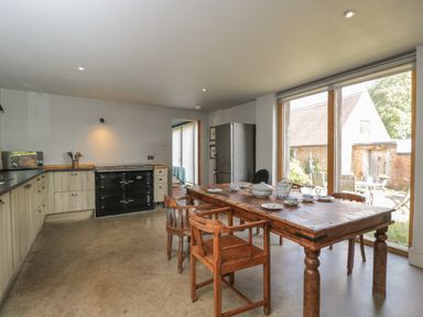 A kitchen with wooden chairs and a table set with dishes next to large windows at Brandeers Long Barn Brandier near Minety