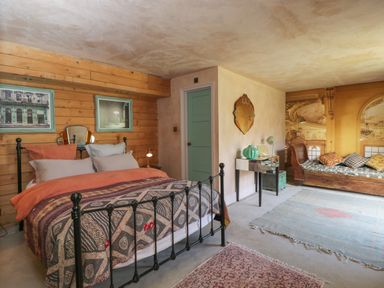 A bedroom with a black metal bed frame, wooden wall, green door, small desk with mirror and green lamp, and wooden sofa with cushions at Brandeers Long Barn in Brandier near Minety