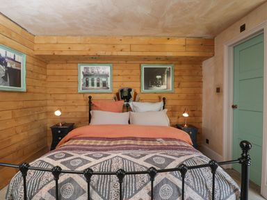 A bedroom with a bed with pillows and blanket wooden walls two side tables with lamps and framed pictures on the wall at Brandeers Long Barn Brandier near Minety
