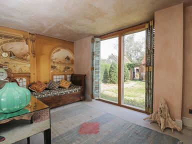 A room with a wooden daybed with cushions a glass table with a green vase and large windows with wooden shutters at Brandeers Long Barn in Brandier near Minety