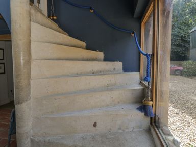 A stone staircase with a blue rope handrail next to a large window showing an outdoor area at Brandeers Long Barn in Brandier near Minety