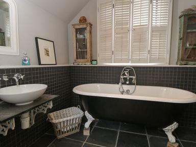 A bathroom with a black and white clawfoot bathtub a white sink a wicker basket and window shutters at Brandeers Long Barn Brandier near Minety