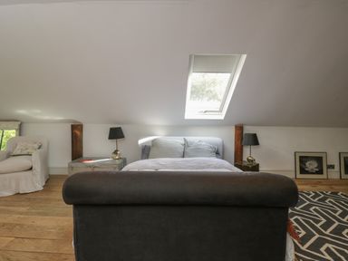 An attic bedroom with a skylight above the bed two bedside tables with lamps and a white armchair near a window at Brandeers Long Barn Brandier near Minety