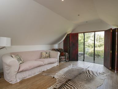 A living area with a sofa, patterned rug, armchair, and glass doors opening to a balcony at Brandeers Long Barn Brandier near Minety