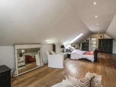 A bedroom with a bed a white armchair a large mirror on the floor and wooden flooring at Brandeers Long Barn Brandier near Minety
