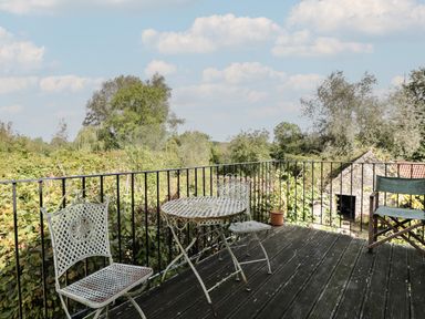 A balcony with metal table and chairs overlooking trees and a stone building at Brandeers Long Barn in Brandier near Minety