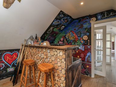 A small bar area with wooden stools and a wall decorated with colorful graffiti at Brandeers Long Barn in Brandier near Minety