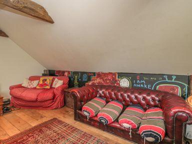 An attic room with a red patterned loveseat and a brown leather sofa with cylindrical pillows at Brandeers Long Barn in Brandier near Minety