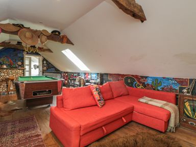 A room with a red sectional sofa a pool table and hats hanging on wooden beams at Brandeers Long Barn Brandier near Minety