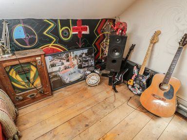 A corner of a room with guitars a wall clock a speaker a vintage radio and a framed photo at Brandeers Long Barn in Brandier near Minety