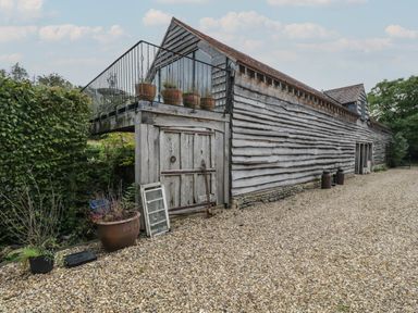 An exterior view of a wooden barn with gravel ground and potted plants at Brandeers Long Barn Brandier near Minety