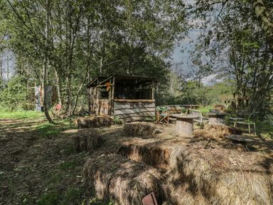 An outdoor bar area with hay bales and wooden spool tables surrounded by trees at Brandeers Long Barn in Brandier near Minety