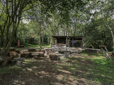 An outdoor bar area with wooden tables metal chairs and hay bale seating under trees at Brandeers Long Barn in Brandier near Minety