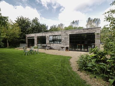 A modern wooden building with large black framed windows and a lawn with garden furniture at The Big Box Brandeers in Brandier near Minety