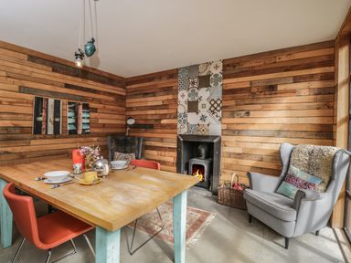 A dining room with a wooden table set for two red chairs a fireplace with patterned tiles and two gray armchairs at The Big Box Brandeers Brandier near Minety