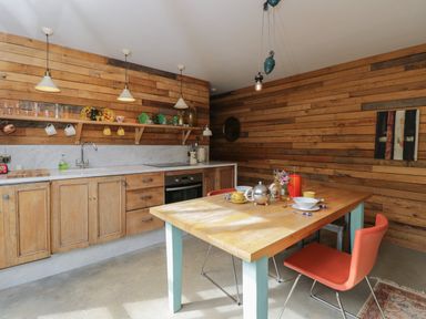 A kitchen with wooden cabinets a dining table set with cups and bowls and red chairs at The Big Box Brandeers Brandier near Minety