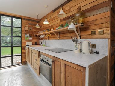 A kitchen with wooden cabinets marble countertop shelves with kitchen items and large window at The Big Box Brandeers in Brandier near Minety