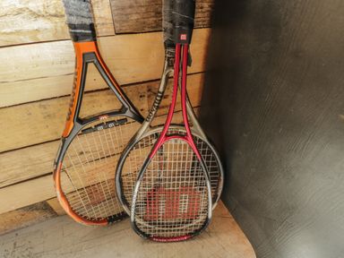 Three tennis rackets leaning against a wooden wall and black surface at The Big Box Brandeers Brandier near Minety