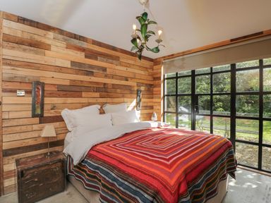 A bedroom with a wooden wall a bed with a red striped blanket and a window overlooking a garden at The Big Box Brandeers Brandier near Minety