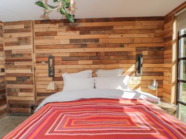 A bedroom with a bed covered by a red striped blanket and wood-paneled walls at The Big Box Brandeers Brandier near Minety