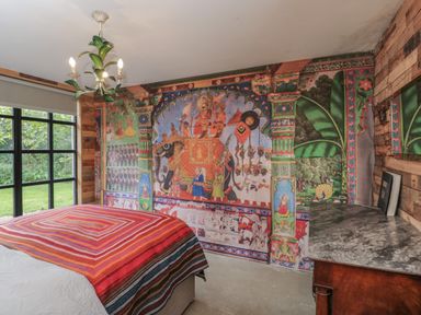 A bedroom with a mural of an elephant procession on one wall a bed with a multicolored striped blanket a wooden dresser with a marble top and a window showing green grass at The Big Box Brandeers Brandier near Minety