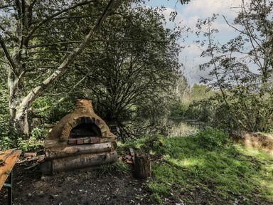 An outdoor area with a stone oven near trees and a pond at The Big Box Brandeers Brandier near Minety